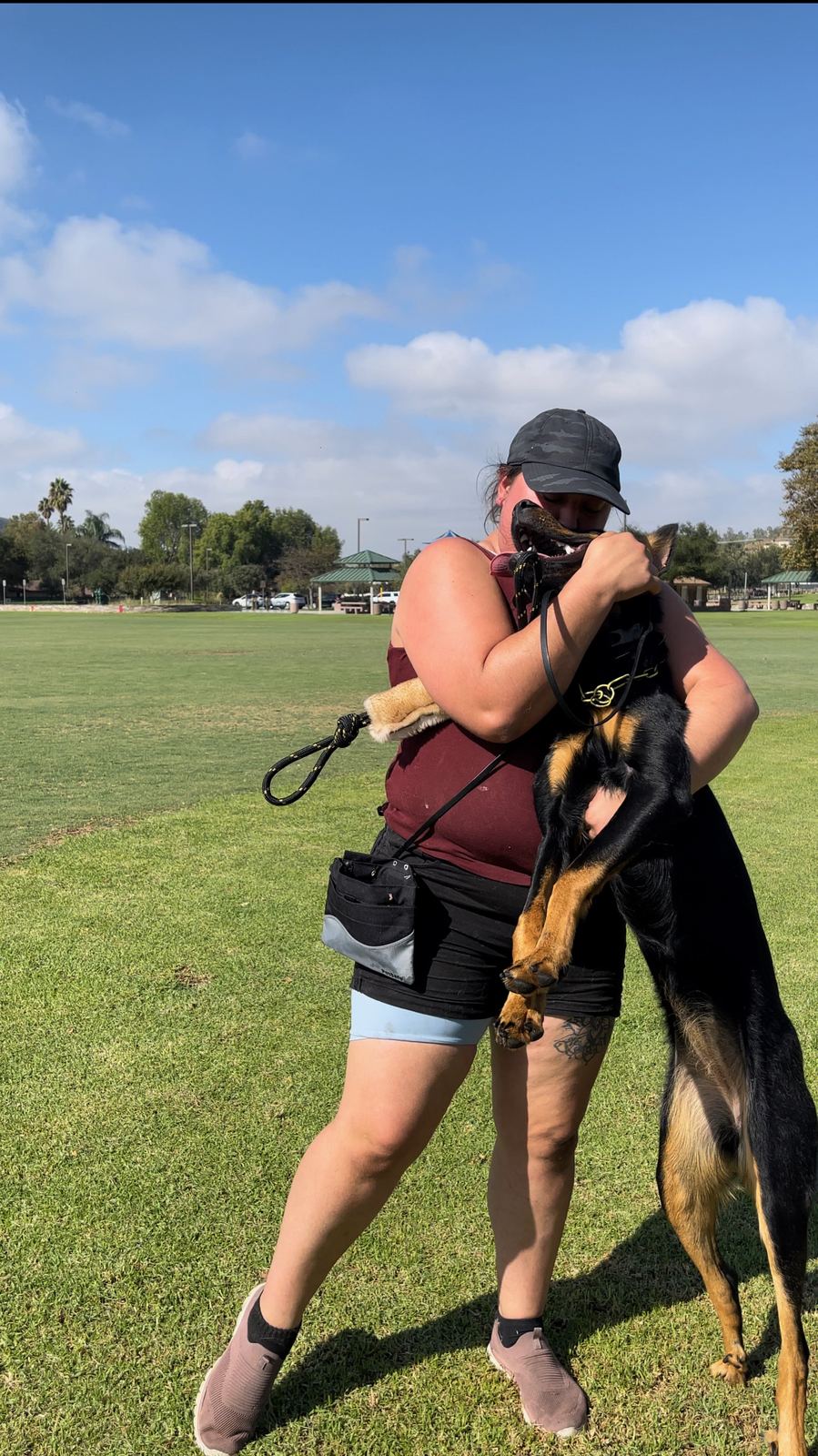 A trainer hugging a shepherd in a sunny park